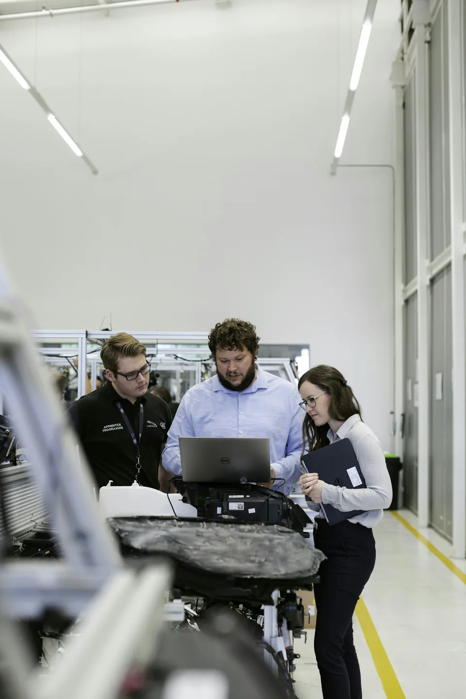 Three engineers reviewing vehicle software beside an automotive prototype